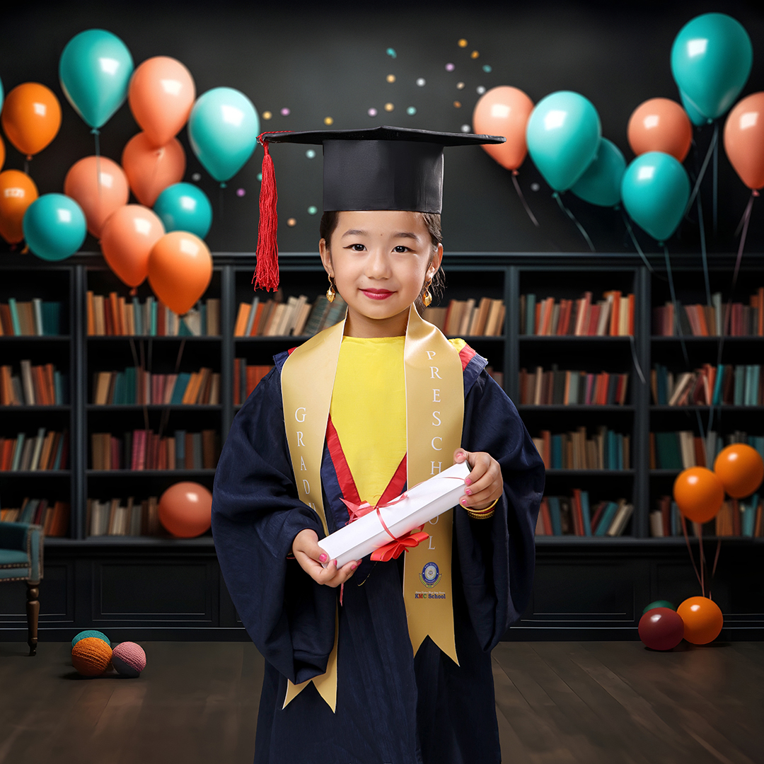 Preschool graduate in cap and gown holding a certificate, Montessori graduation photo recreated in studio with bookshelf and colorful balloons in background.