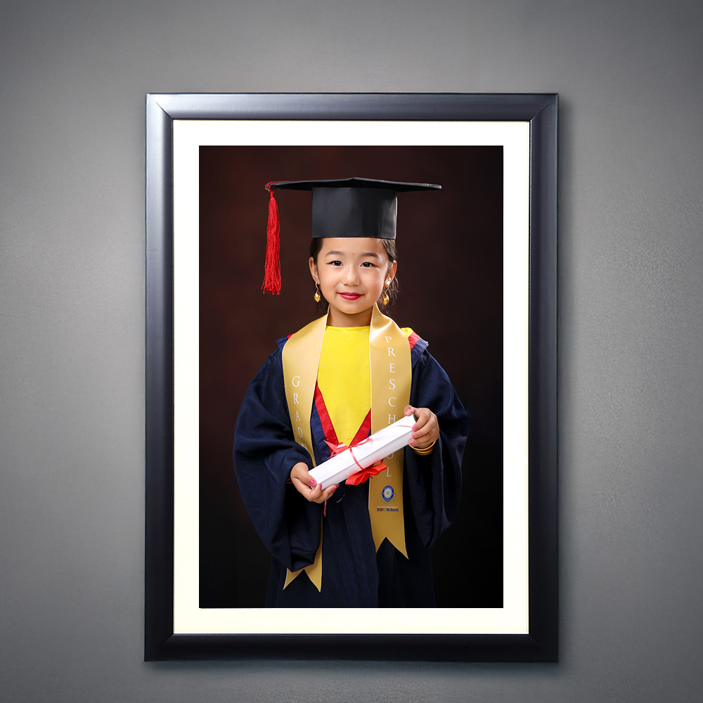 Smiling young child in graduation gown and cap holding certificate at Graduation Photo Studio
