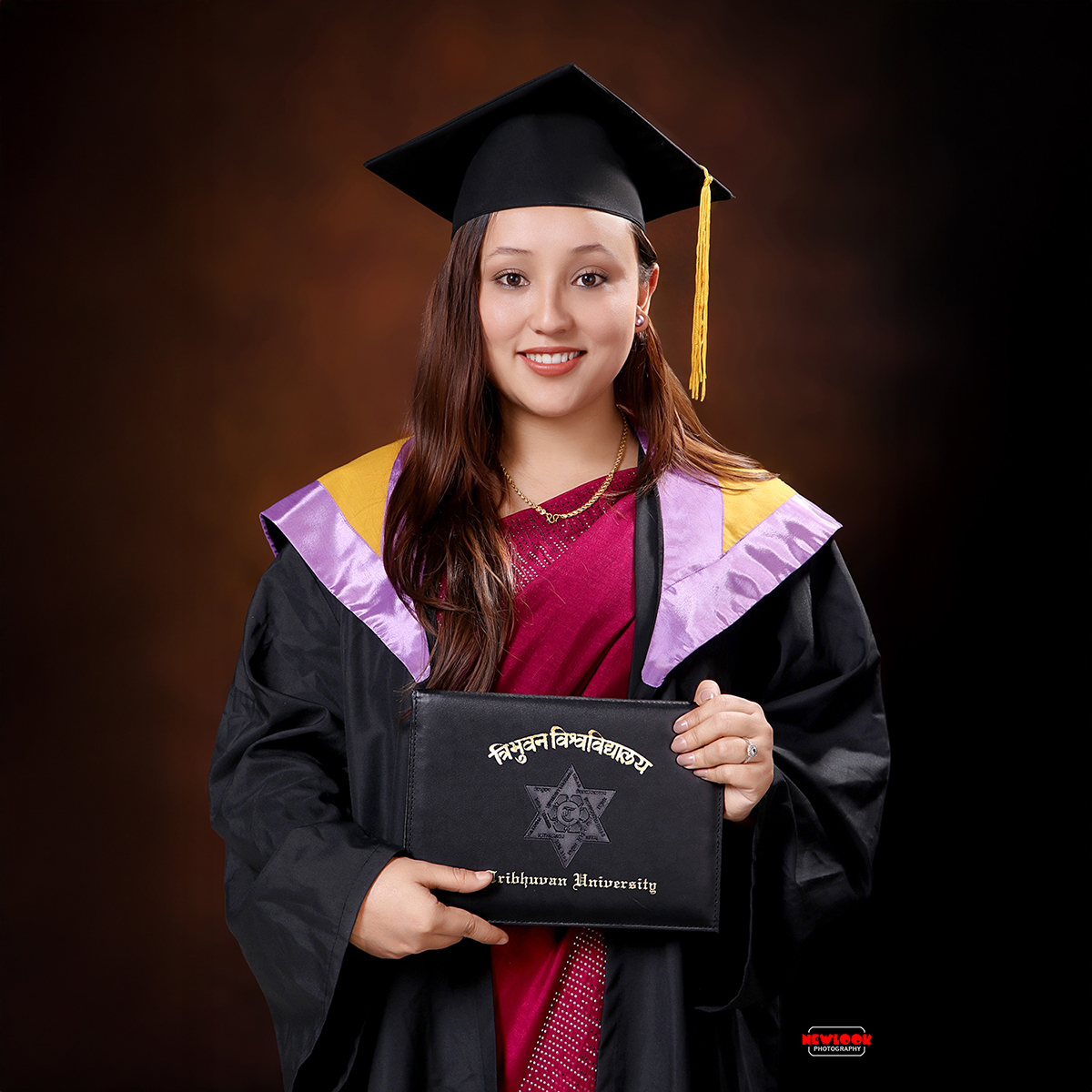 Smiling young lady in graduation gown and cap holding TU certificate in graduation backdrop in Graduation Photo Studio