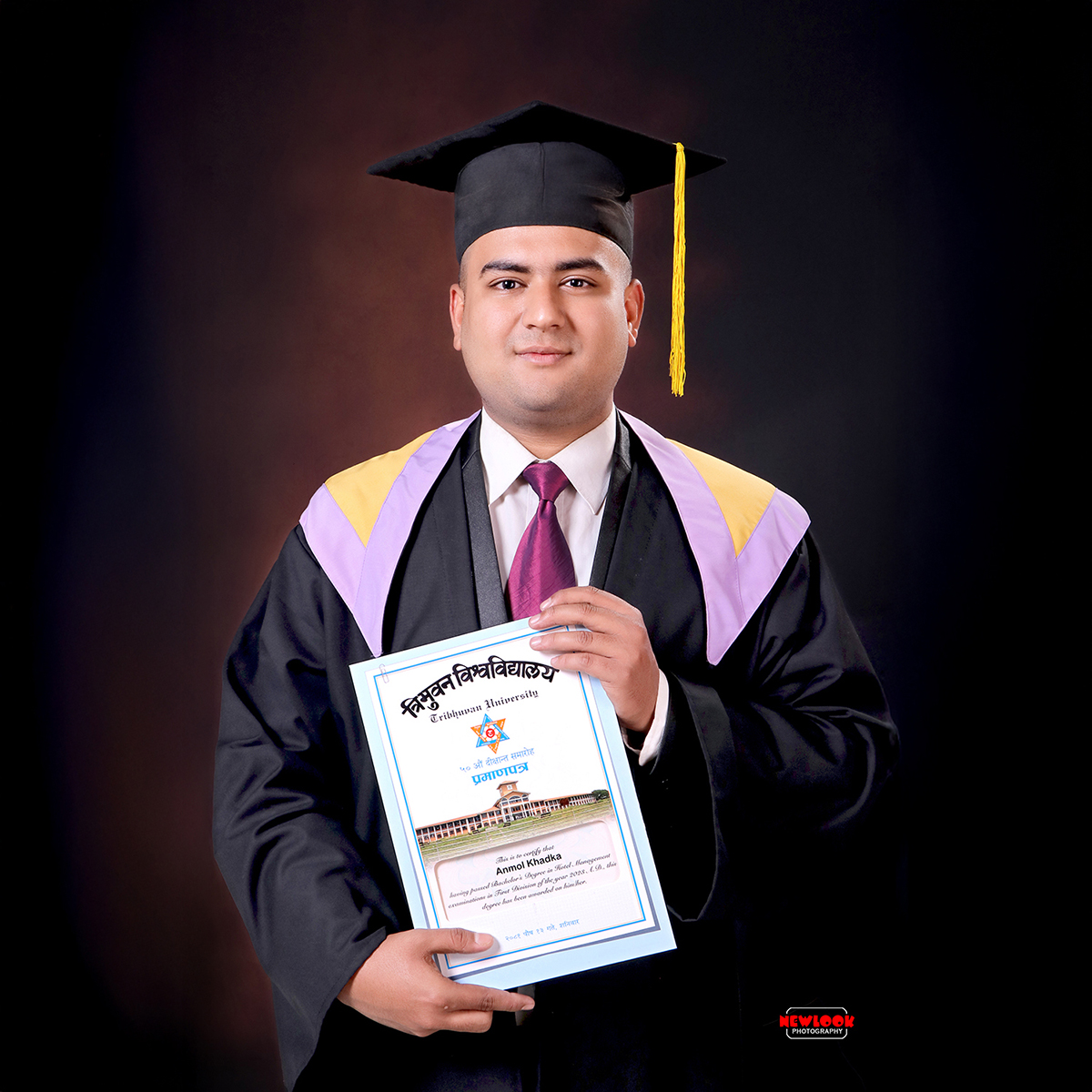 Smiling young man in graduation gown and cap holding TU certificate in graduation backdrop in Graduation Photo Studio