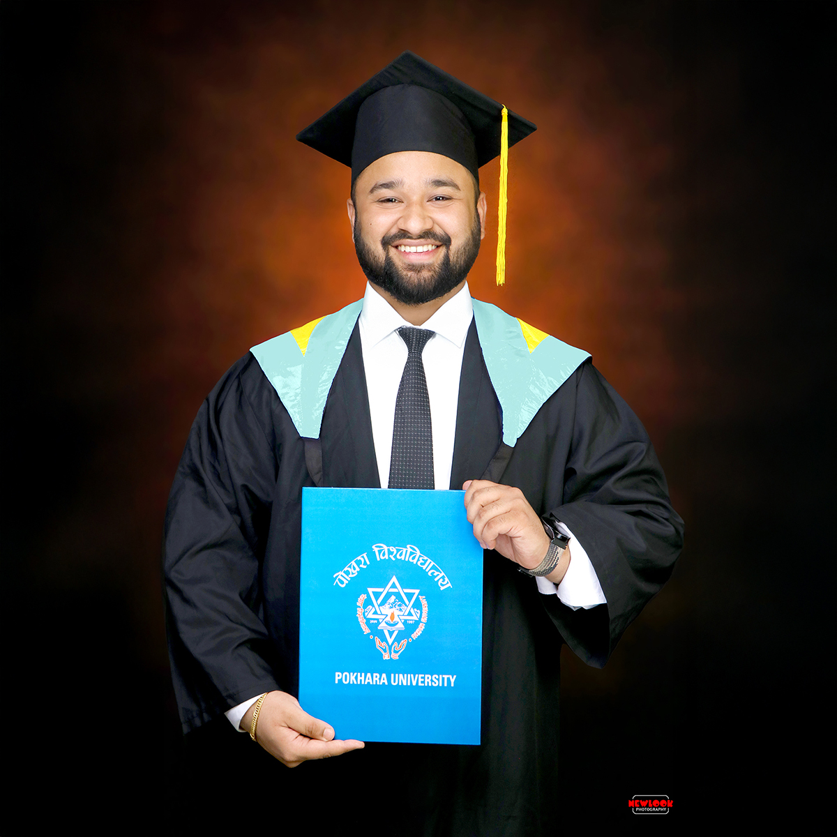 Smiling young man in graduation gown and cap holding Pokhara certificate in graduation backdrop in Graduation Photo Studio